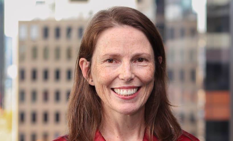 Elanor is smiling broadly at the camera. She has auburn hair, brown eyes and pale skin with freckles. She's wearing a deep red shirt.